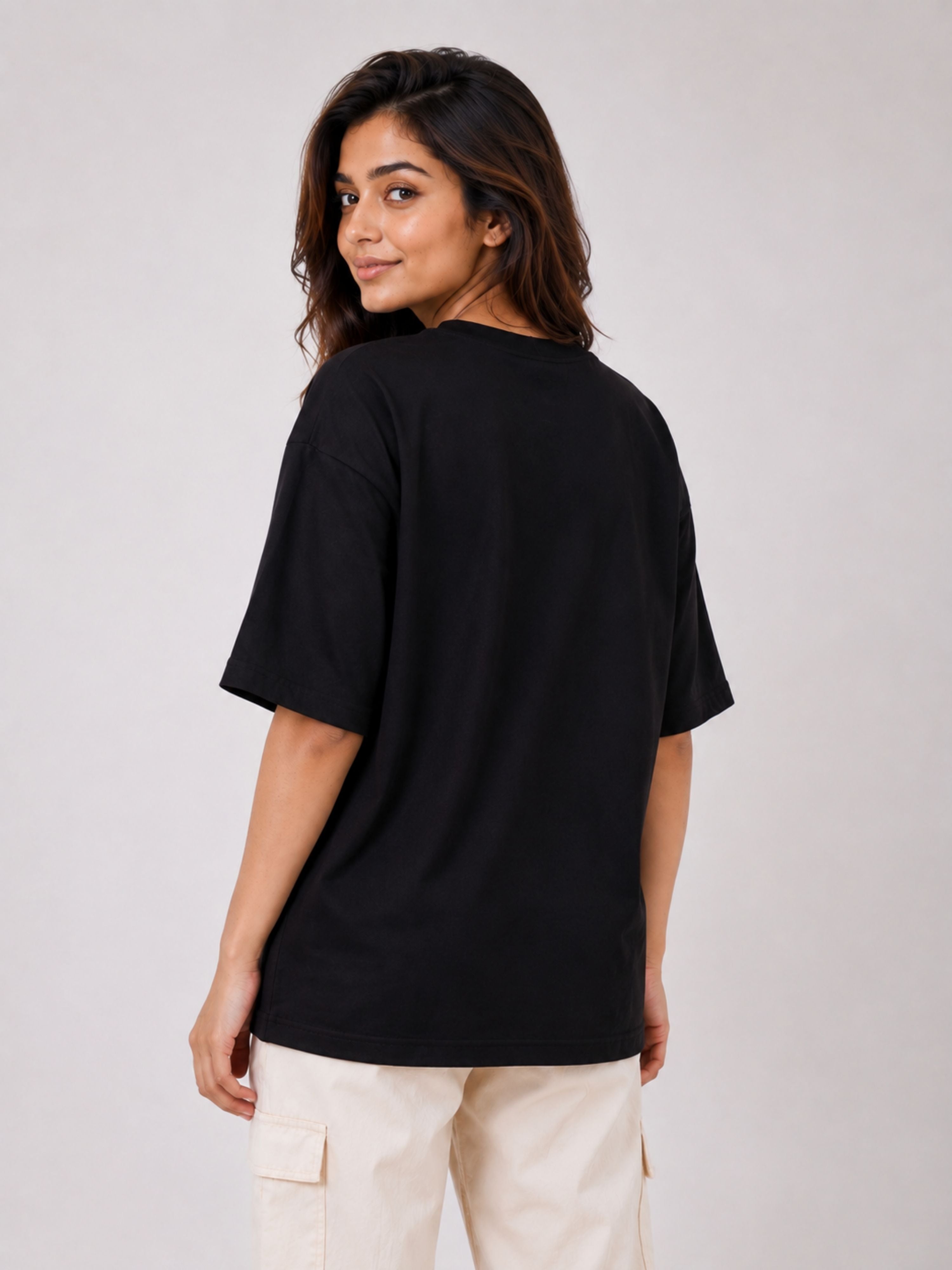 Back view of a woman wearing oversized black Journalists Quote T-shirt For Women paired with beige cargo pants