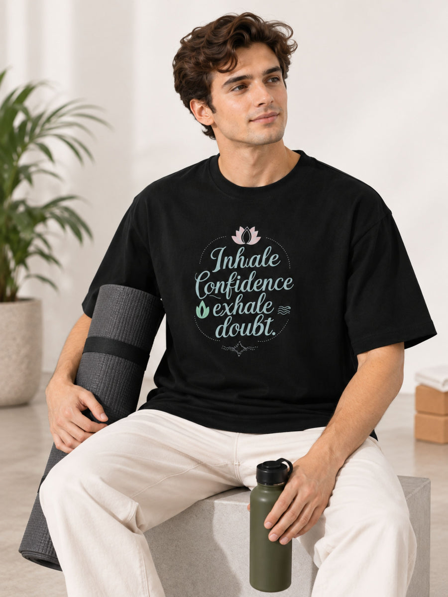 Black oversized fit Yoga Instructor Tshirt For Men with inhale confidence design worn by man holding yoga mat and water bottle